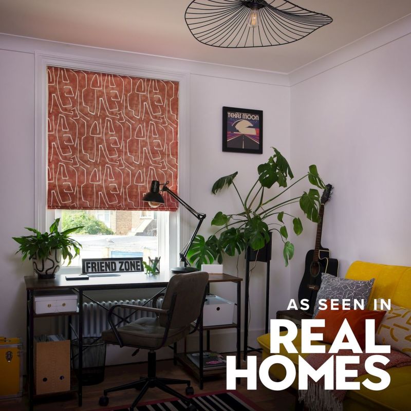 Patterned fabric Roman blind (rust with white abstract-line motif) lowered, filtering daylight; small home-office corner with desk, lamp, plants, guitar and a yellow sofa.

TEXAS MOON
FRIEND ZONE
AS SEEN IN
REAL HOMES