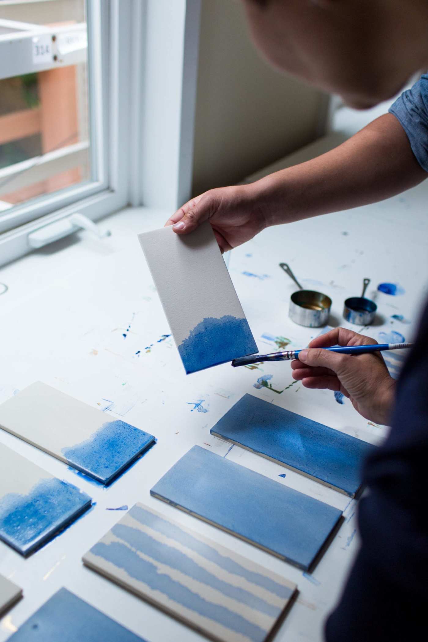 a woman is painting blue tiles on a table.