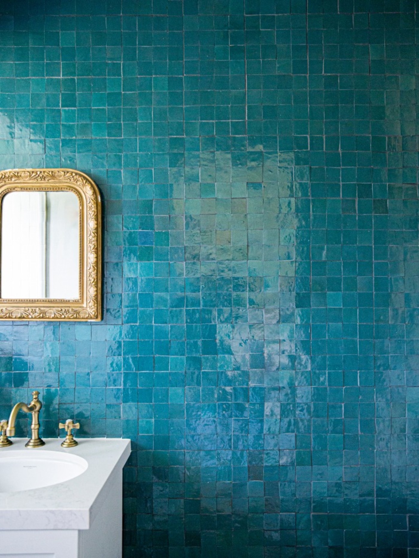 a blue tiled bathroom with a gold mirror.