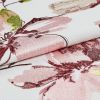 Embroidered floral fabric, white base with pink and burgundy satin-like stitching, folded to reveal raised texture and sheen; close-up studio-lit detail emphasizing pattern and weave.
