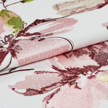 Embroidered floral fabric, white base with pink and burgundy satin-like stitching, folded to reveal raised texture and sheen; close-up studio-lit detail emphasizing pattern and weave.