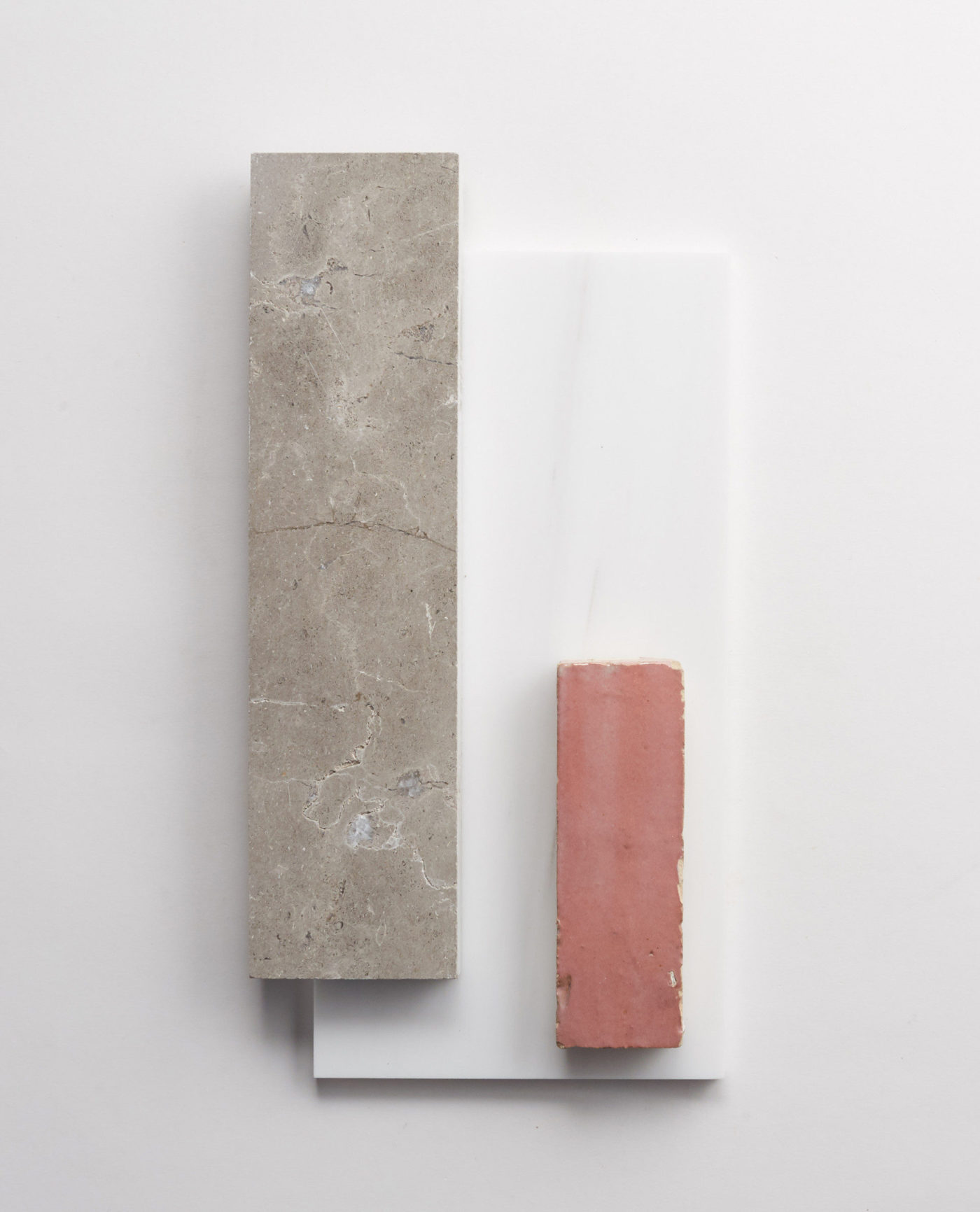 a grey rectangle and pink rectangle tile sitting on top of a white rectangular tile.