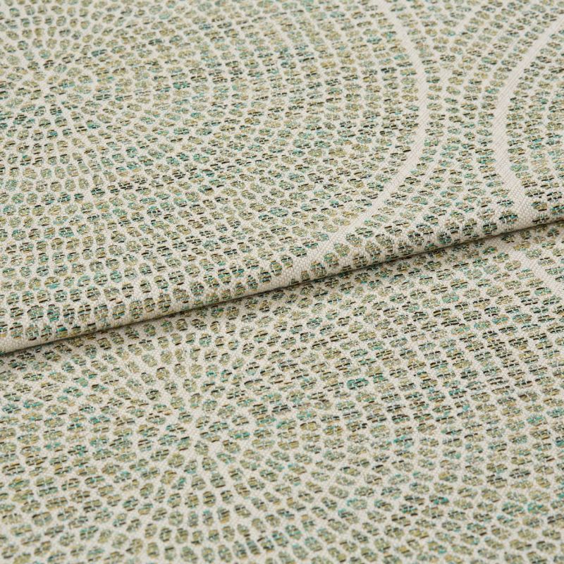 Woven upholstery fabric with small grid and concentric circular motif, folded to show layered edge and textured weave, close-up on a flat surface under soft, neutral lighting.