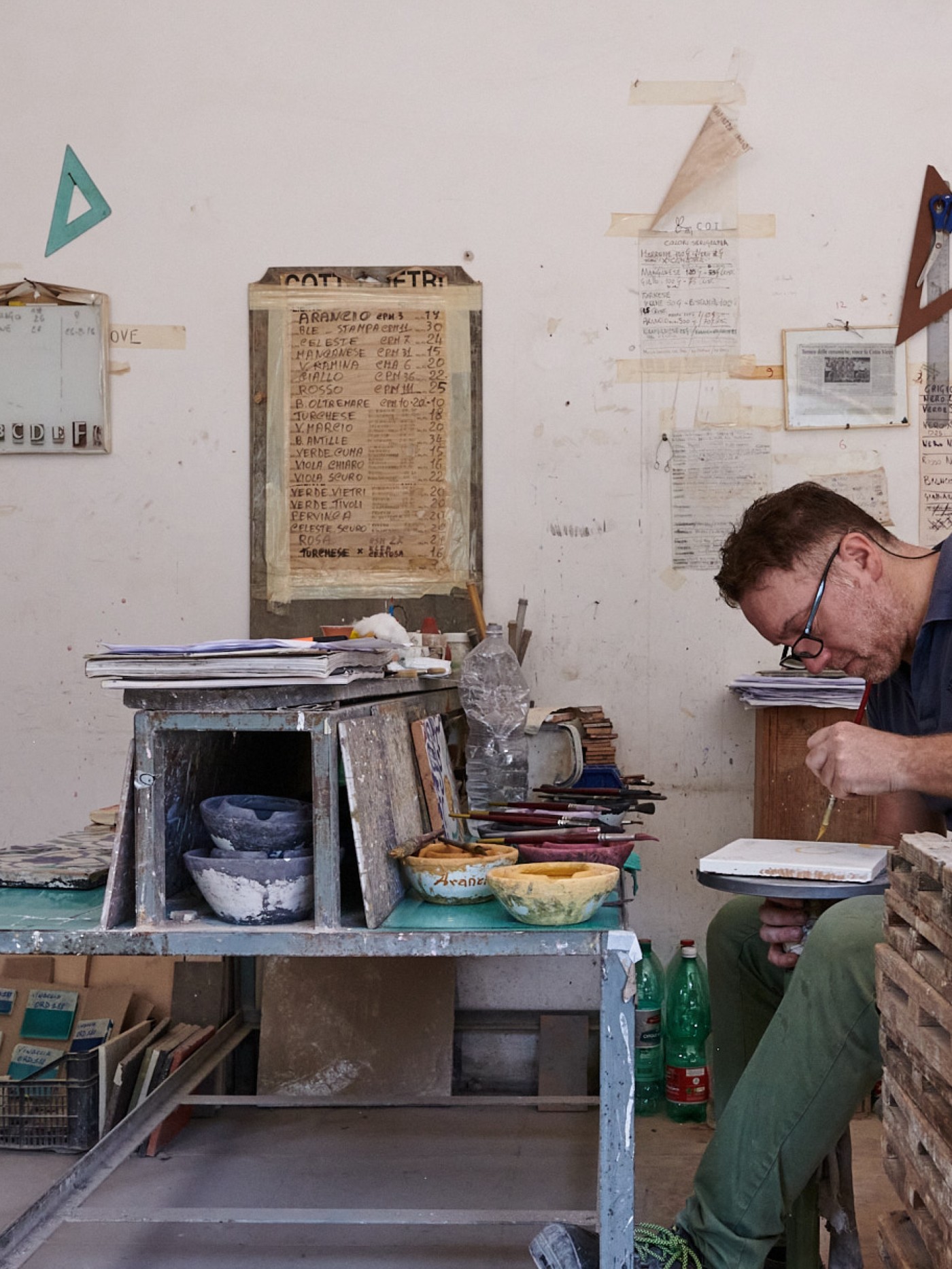 a man hand painting a tile in a workshop.