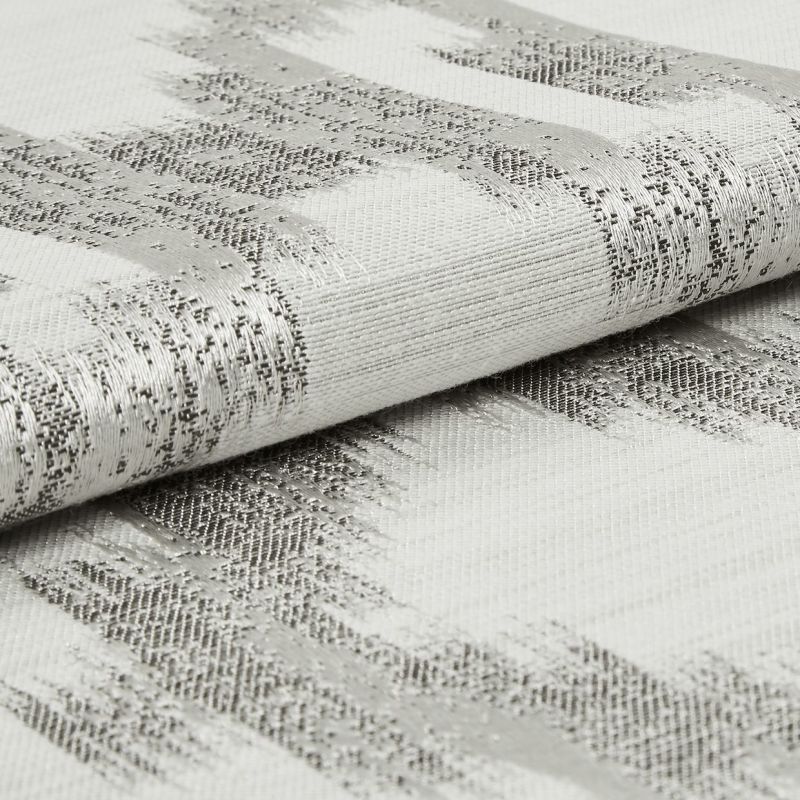Folded woven fabric with silver metallic horizontal stripes, tightly textured and slightly rolled; resting on a matching fabric surface in soft, neutral studio lighting, close-up detail.