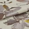 Folded jacquard fabric with large metallic floral motifs in mauve, grey and yellow on a cream ground; folded edge overlapping, catching light; close-up textile sample under soft, even lighting.