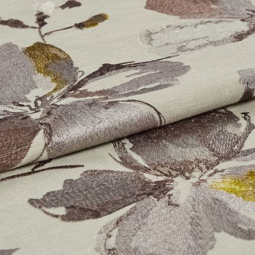 Folded jacquard fabric with large metallic floral motifs in mauve, grey and yellow on a cream ground; folded edge overlapping, catching light; close-up textile sample under soft, even lighting.