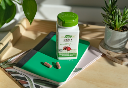A bottle of Beet Root on a green notebook next to two capsules and a potted succulent.