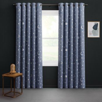 Grommet-top navy curtains patterned with moons and stars, hung on a metal rod, parted to admit soft daylight; dark-painted room with wooden side table, dome lamp, abstract print.