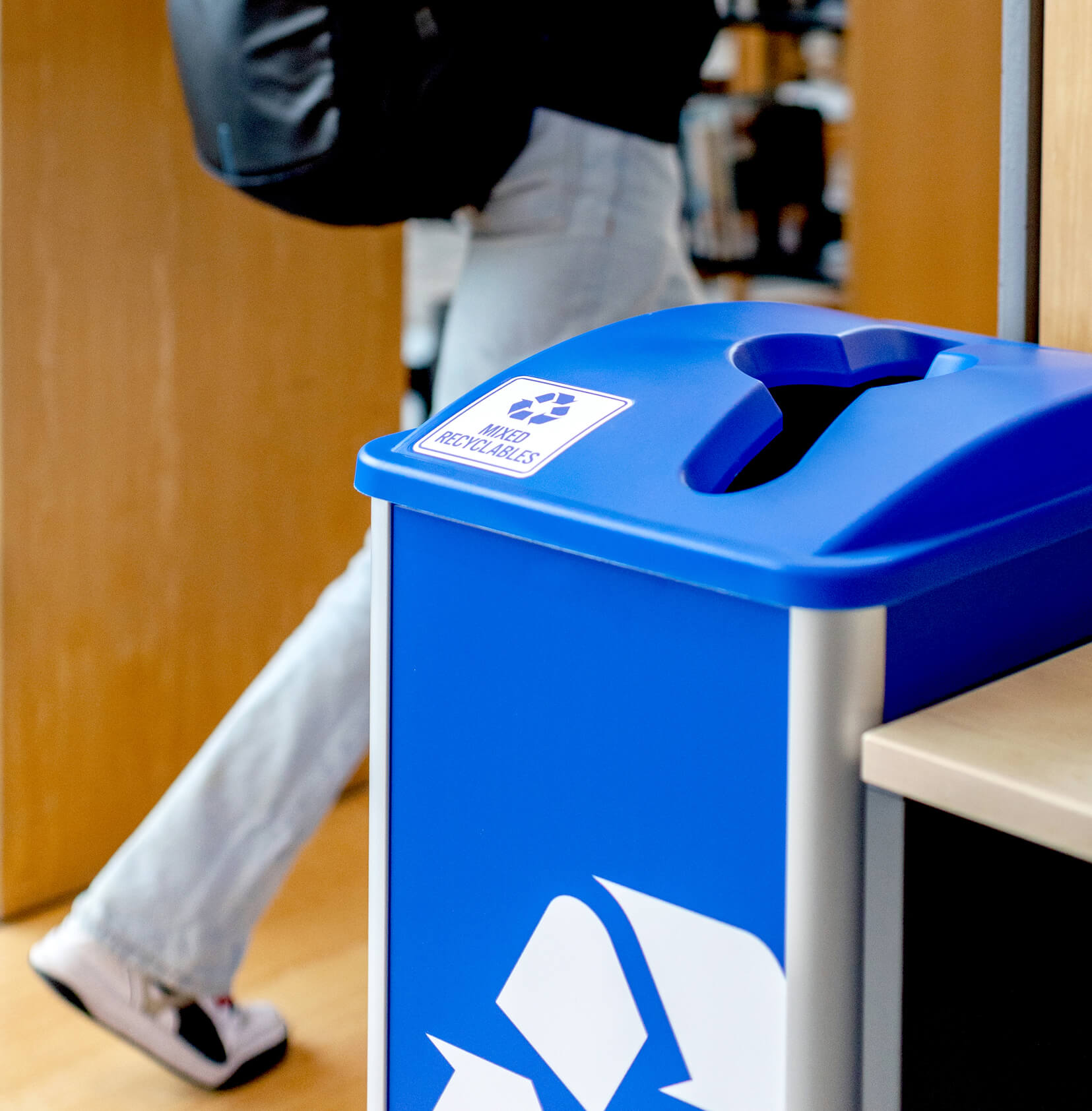 recycling container in a college library with a student walking by