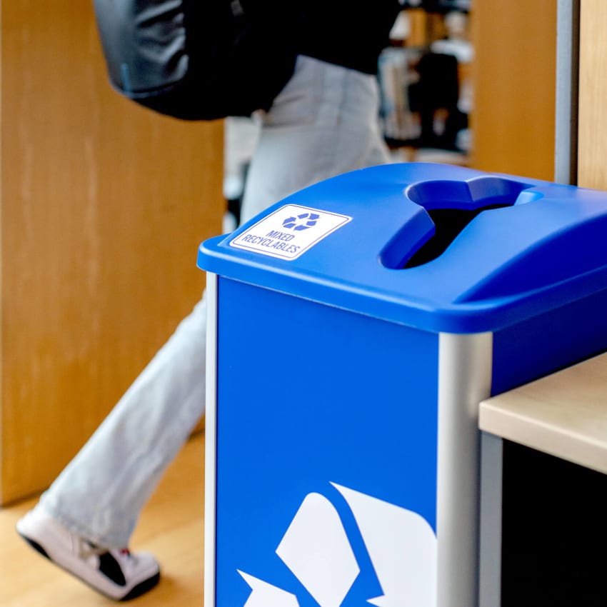 recycling container in a college library with a student walking by