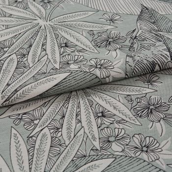 Folded floral-patterned fabric with leaf and flower print positioned diagonally, layered and partially overlapped; black outlined botanical motifs on a pale mint background, photographed close-up in soft lighting.