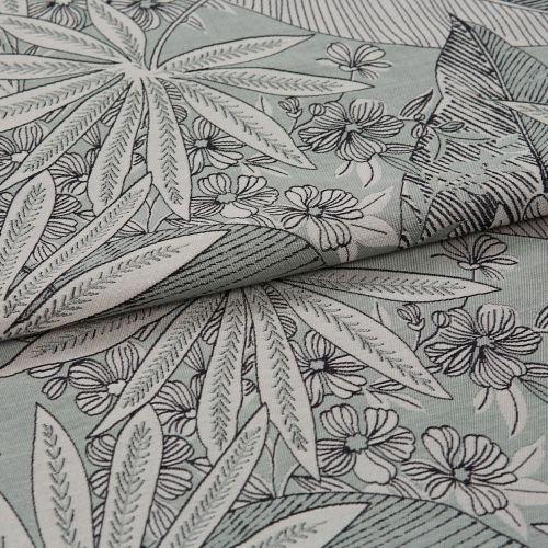 Folded floral-patterned fabric with leaf and flower print positioned diagonally, layered and partially overlapped; black outlined botanical motifs on a pale mint background, photographed close-up in soft lighting.