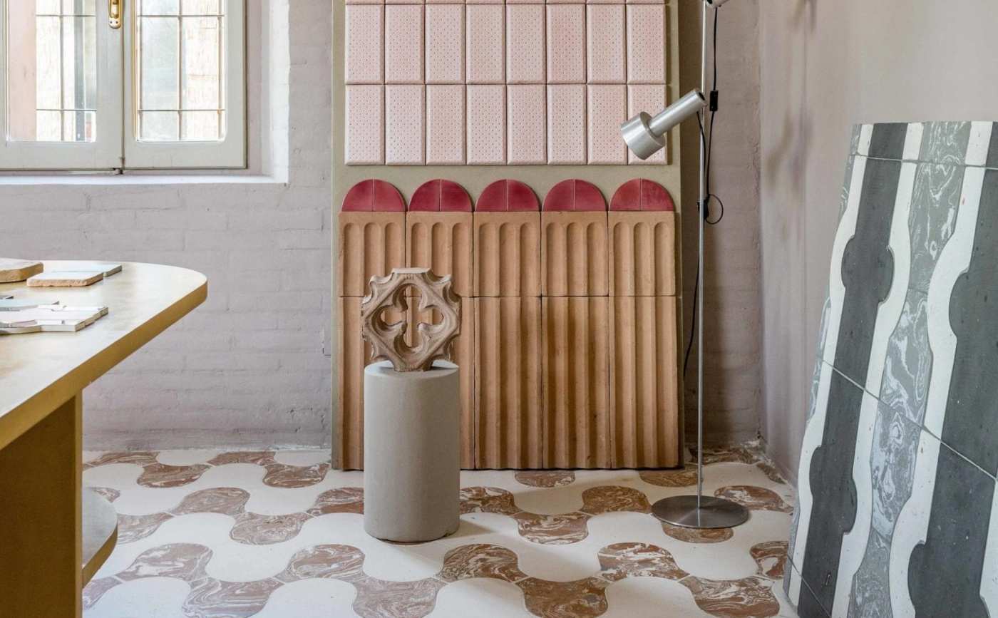 a room with a pink and white tiled floor, a wooden table, and various other tiles laying around.