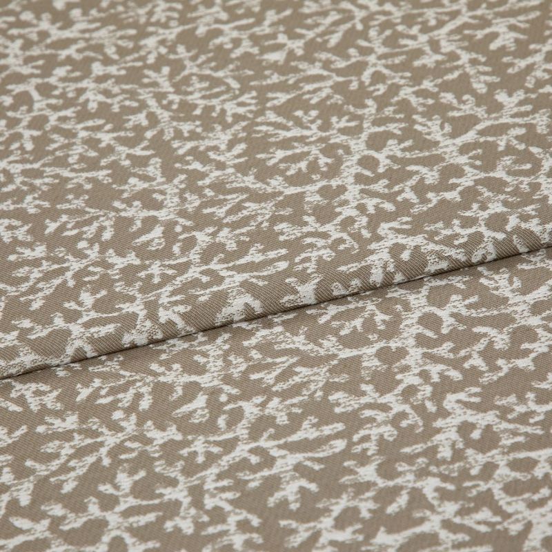 Beige woven fabric with a white, branch-like pattern folded across itself, shown close-up on a flat surface under soft, even lighting.