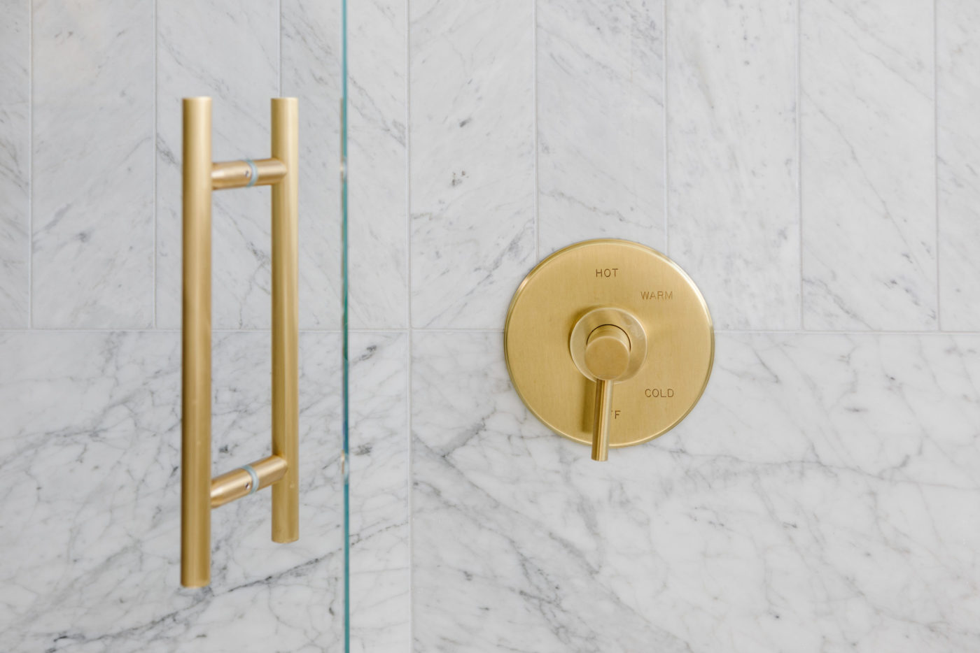 a brass shower handle on a marble wall.