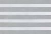 A dual-layer zebra roller blind with alternating opaque white and sheer gray textured horizontal bands across the window; filtering and diffusing daylight while partially blocking view; neutral indoor lighting.