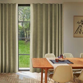 Floor-length, green-and-cream checkered curtains flanking a tall divided window, partially drawn and filtering daylight; dining table and chairs in foreground, hardwood herringbone floor, garden with grass and trees visible.
