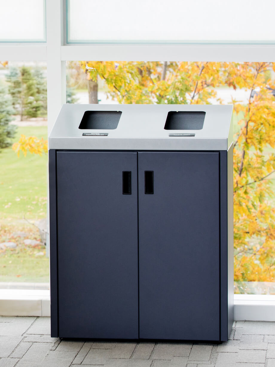 double powder coated metal recycling and trash bin with a sloped lid and hinged front doors in a college campus lounge
