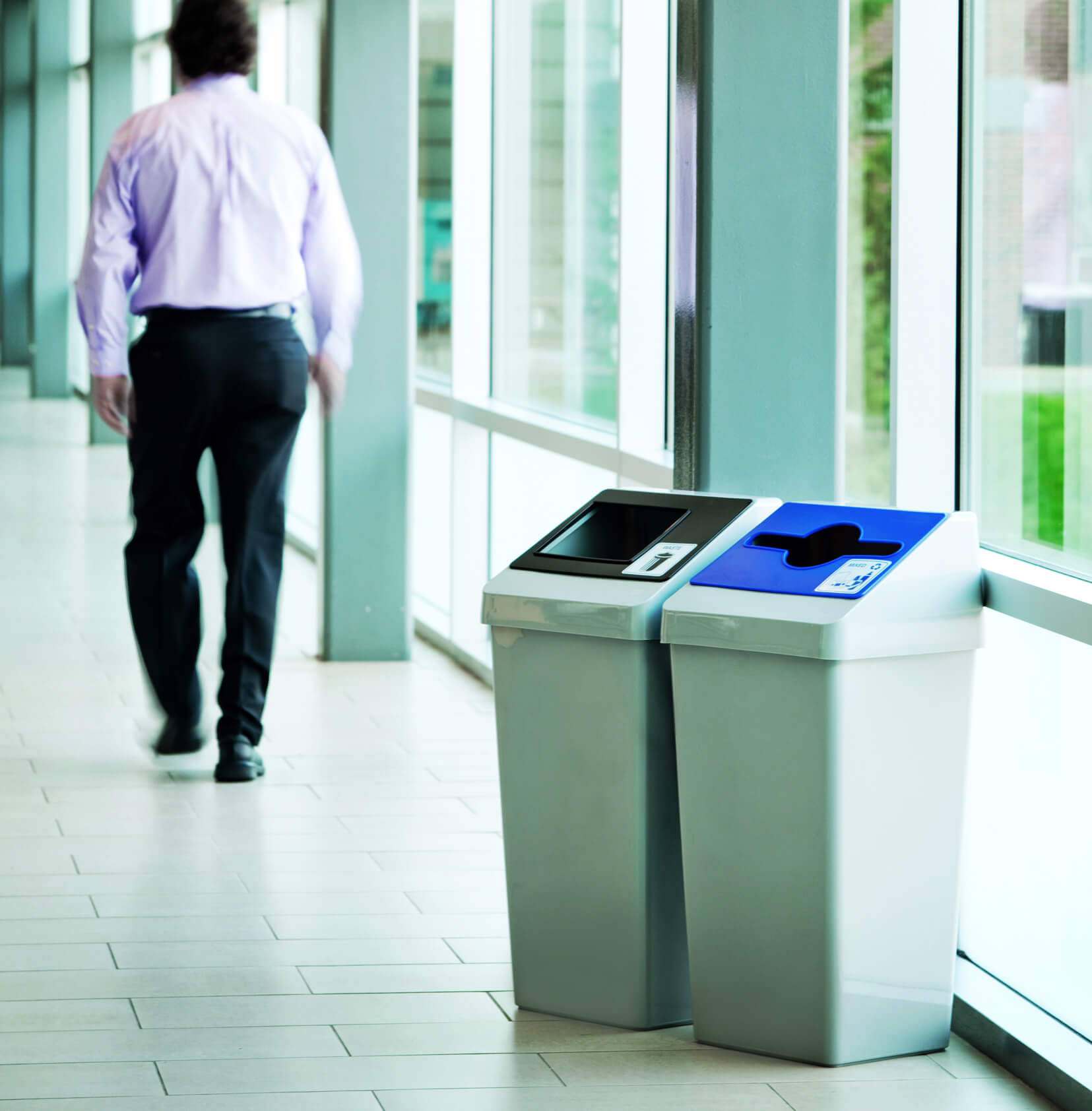 grey plastic waste and recycling bins with color coded restrictive openings in a hospital hallway