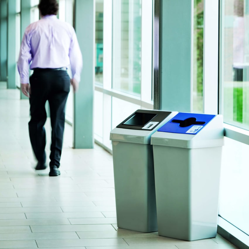 grey plastic waste and recycling bins with color coded restrictive openings in a hospital hallway