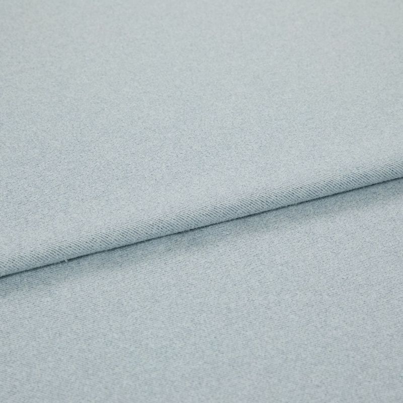 Pale blue woven fabric folded into overlapping layers; diagonal fold runs across frame, showing fine twill-like weave and subtle speckling under soft, even studio lighting.