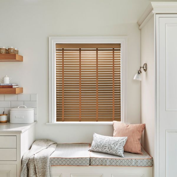 Wooden horizontal slatted blinds in the window, closed and filtering warm daylight; cozy kitchen nook with cushioned bench, neutral cabinetry, shelves and a wall sconce.
BREAD