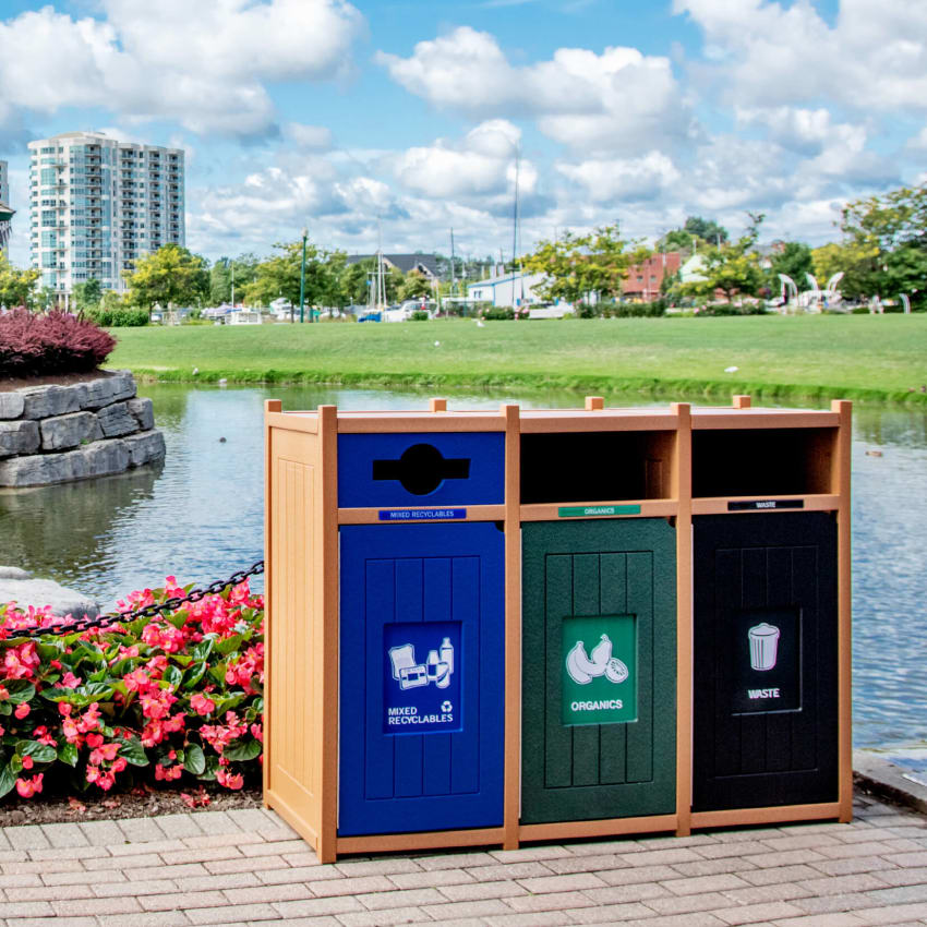 triple mixed recyclables organics and waste container at a municipal park on a sunny day in front of a pond