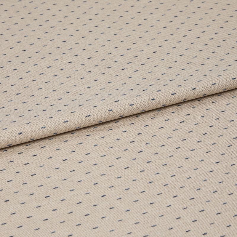 Beige woven fabric with regular small navy dash dots, folded once across center, lying flat on a neutral surface; close-up, even studio lighting highlighting its textured weave.