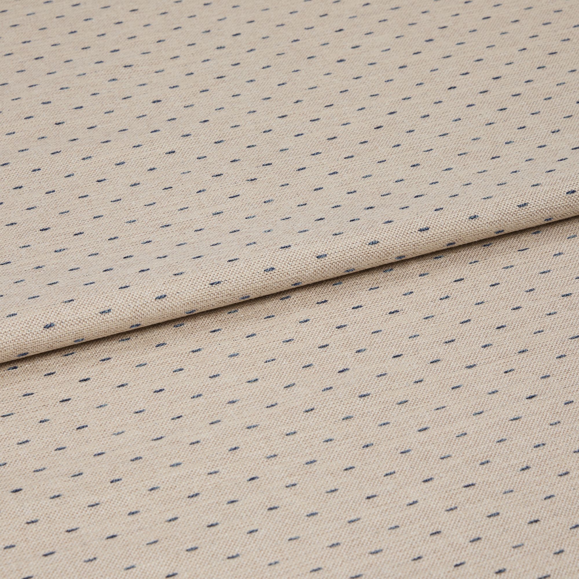 Beige woven fabric with regular small navy dash dots, folded once across center, lying flat on a neutral surface; close-up, even studio lighting highlighting its textured weave.