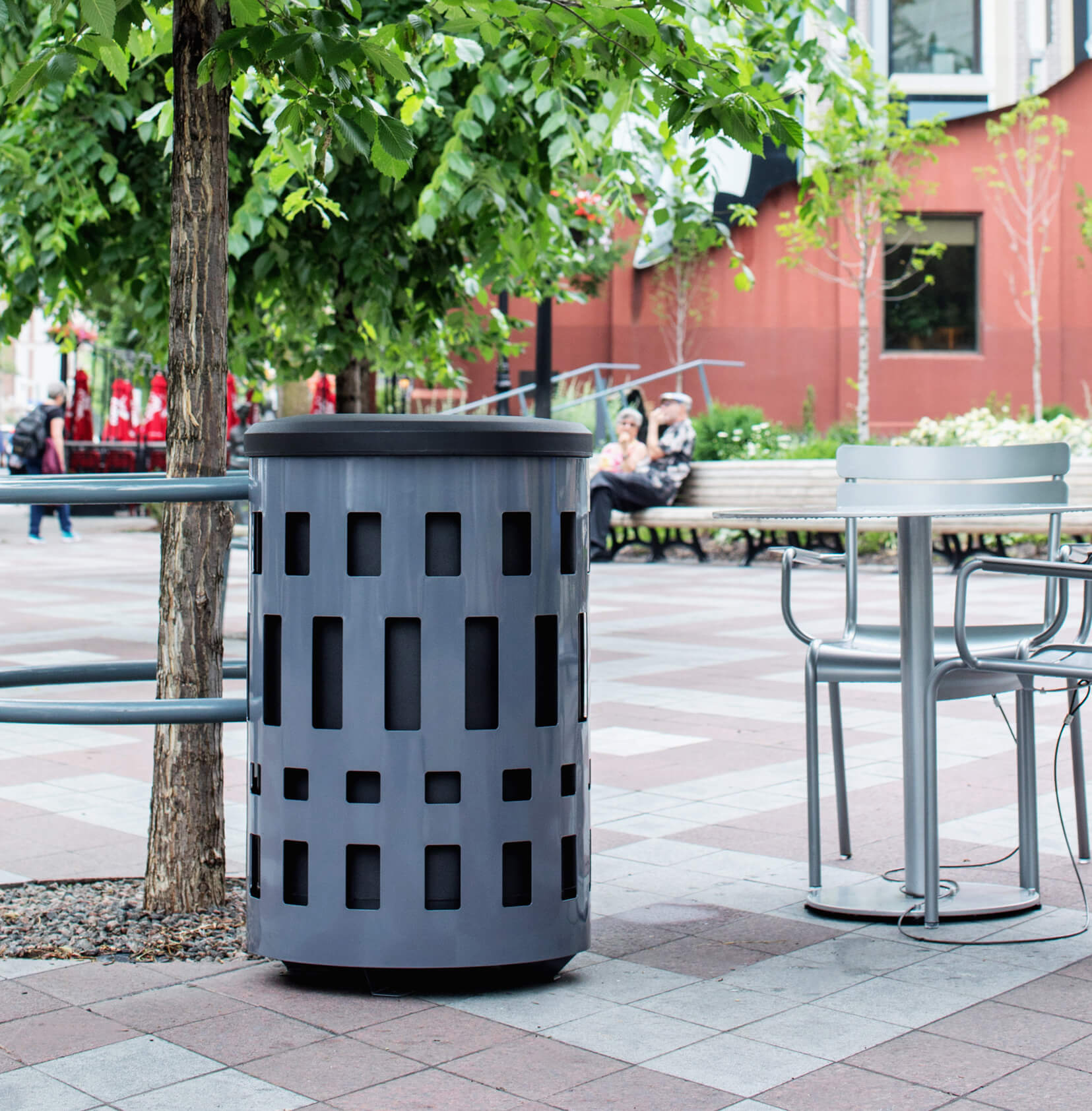 grey powder coated steel outdoor waste container with black plastic lid outside at a city cafe
