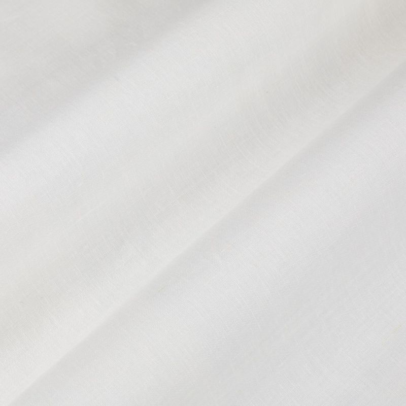 White fabric with a diagonal fold forming a soft shadowed ridge; light subtly diffused across its smooth woven texture in a bright, minimal interior.