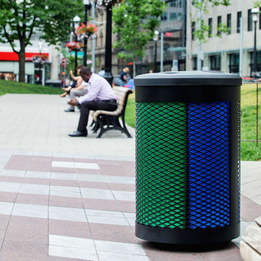 durable steel and plastic outdoor recycling and waste container with color-coded liners in a city park with a man sitting on a bench