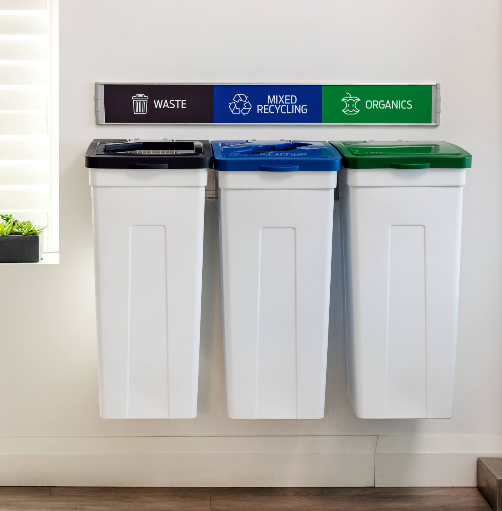 triple wall hanging waste and recycling containers with white bodies and colored lids in a modern office environment