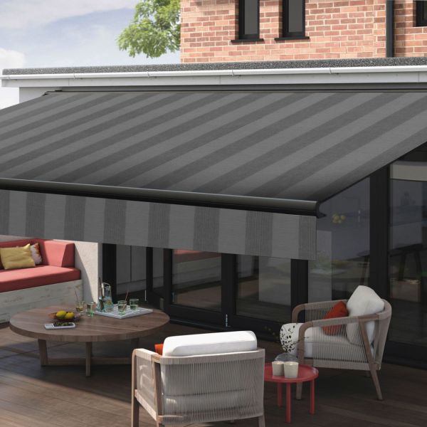 Striped retractable awning (dark gray, diagonal stripes, drop valance) extended over a patio, shading glass doors and outdoor seating on a wooden deck in daylight.