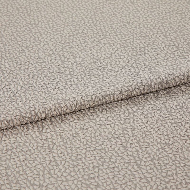 Beige jacquard-like upholstery fabric, folded over itself, displaying a dense small pebble motif; close-up studio-lit view highlighting subtle sheen, woven texture, and gentle drape.