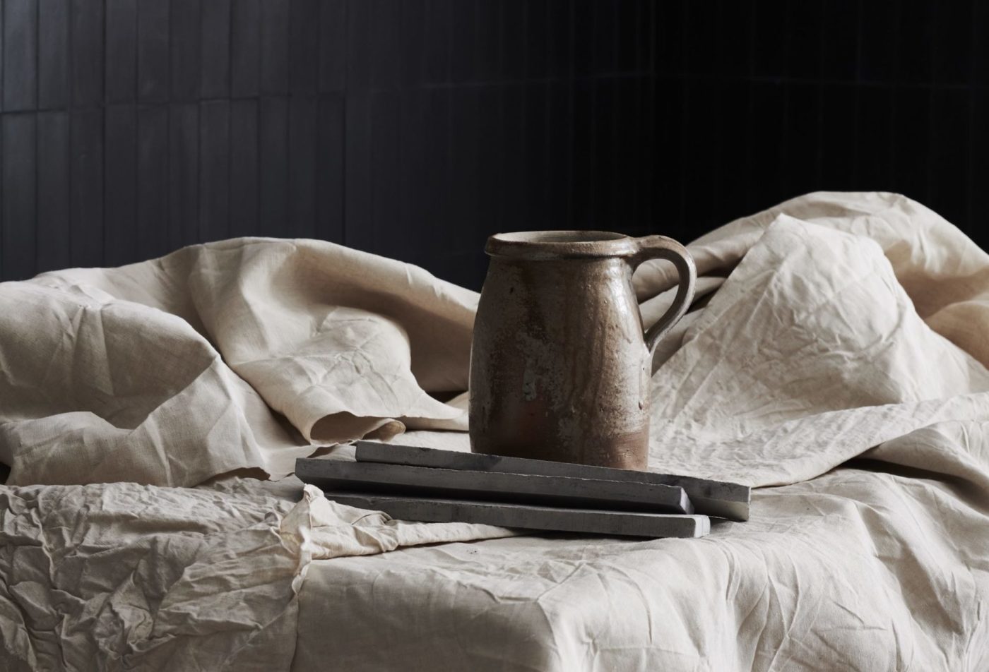 a metal pitcher and several grey tiles on a white sheet.