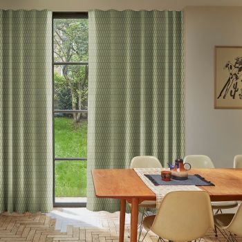 Green patterned curtains, floor-length on each side of a tall three-pane window, hanging in soft folds, partially open and filtering daylight; dining room with wooden table, chairs, garden view.