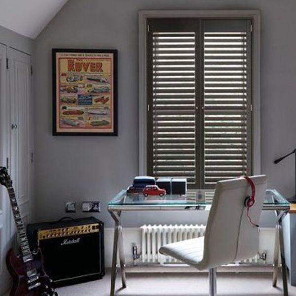 Wooden interior plantation shutters cover a double window, closed with slats angled to filter daylight; set above a glass desk in a grey home office with a chair, guitar and amplifier.
ROVER
Marshall
