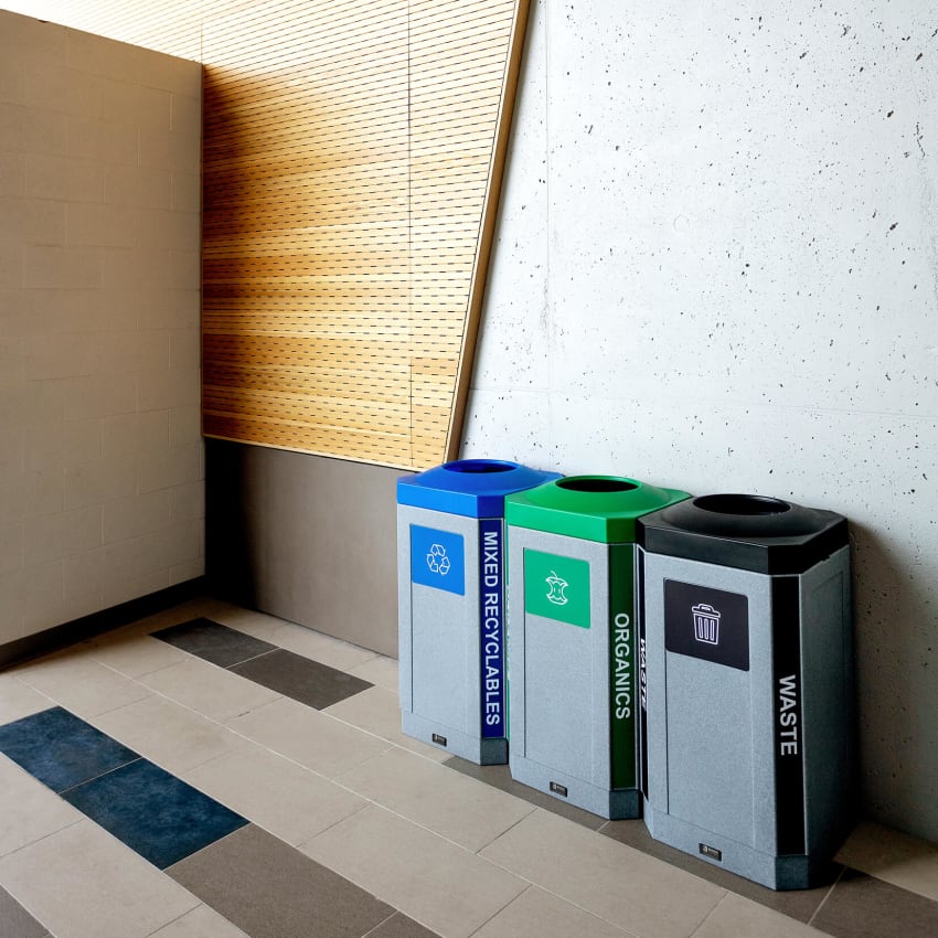 grey plastic triple waste recycling and organics containers with colored lids and labels in a modern college campus