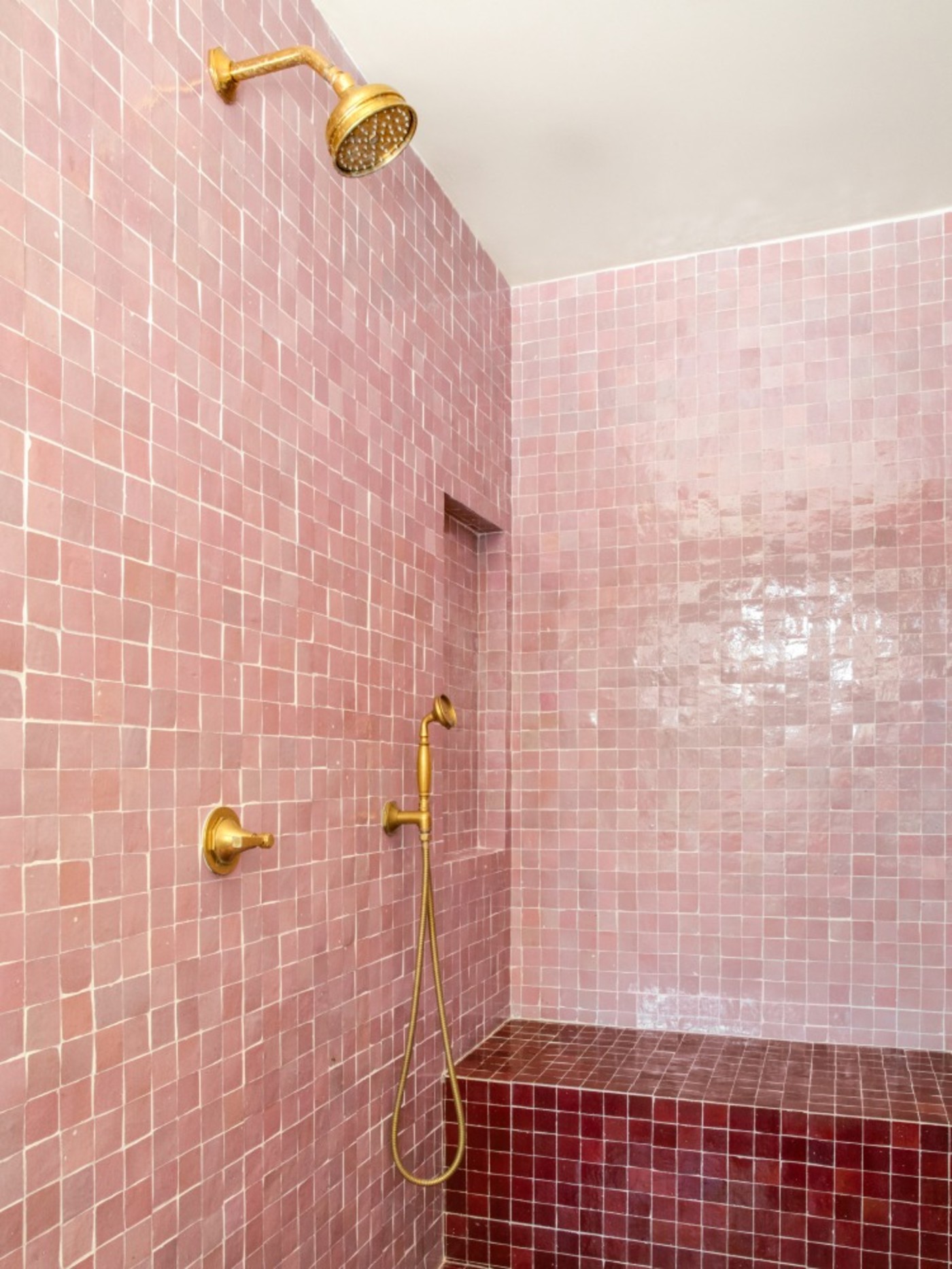 a pink tiled shower with a gold shower head.