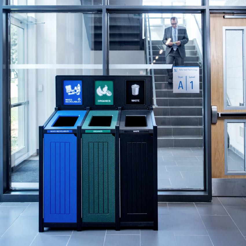 triple recycling organics and waste bin against a glass wall in a modern office with man walking down staircase