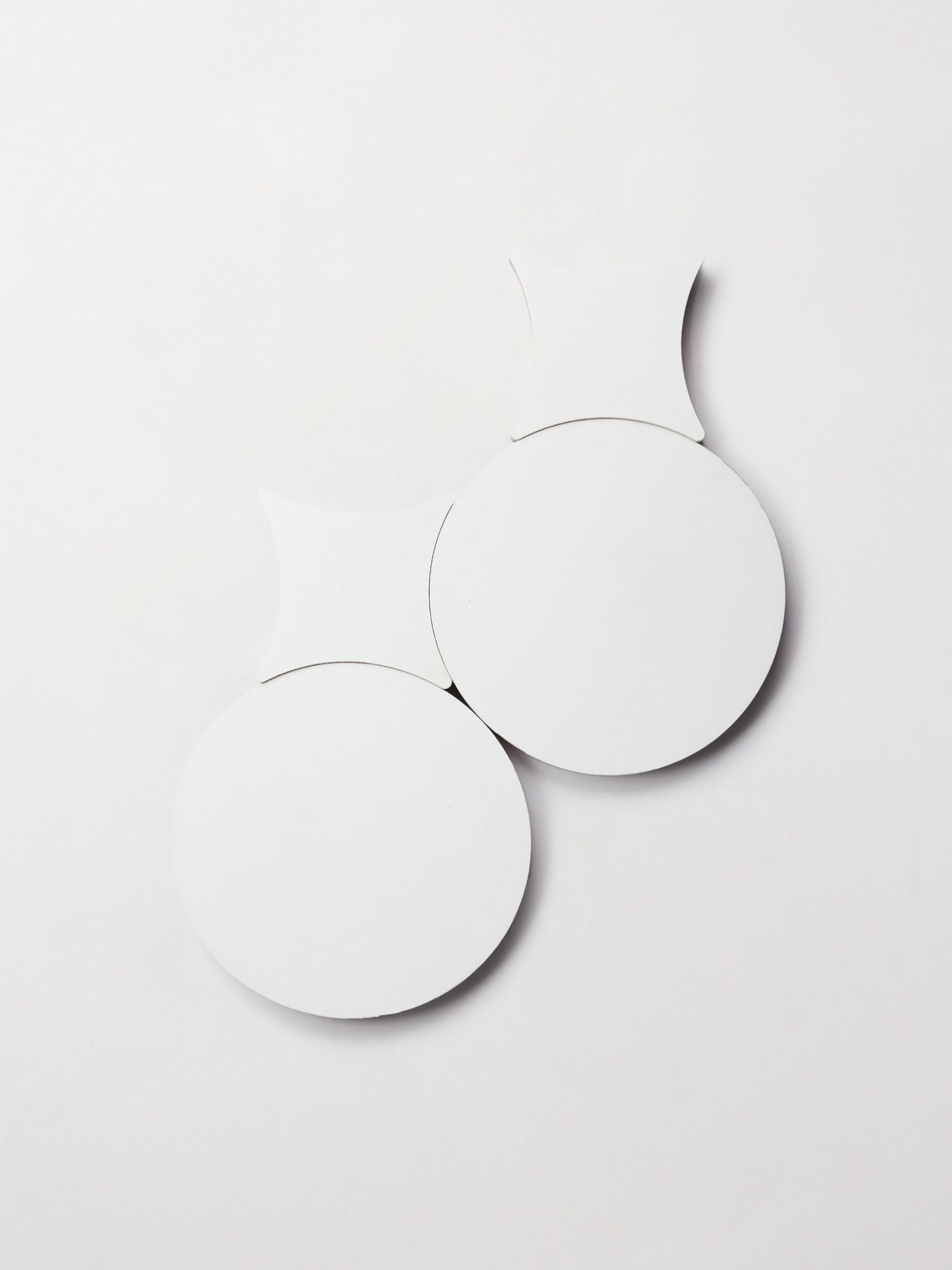 two white circular tiles and two white cross-shaped tiles on a white surface.