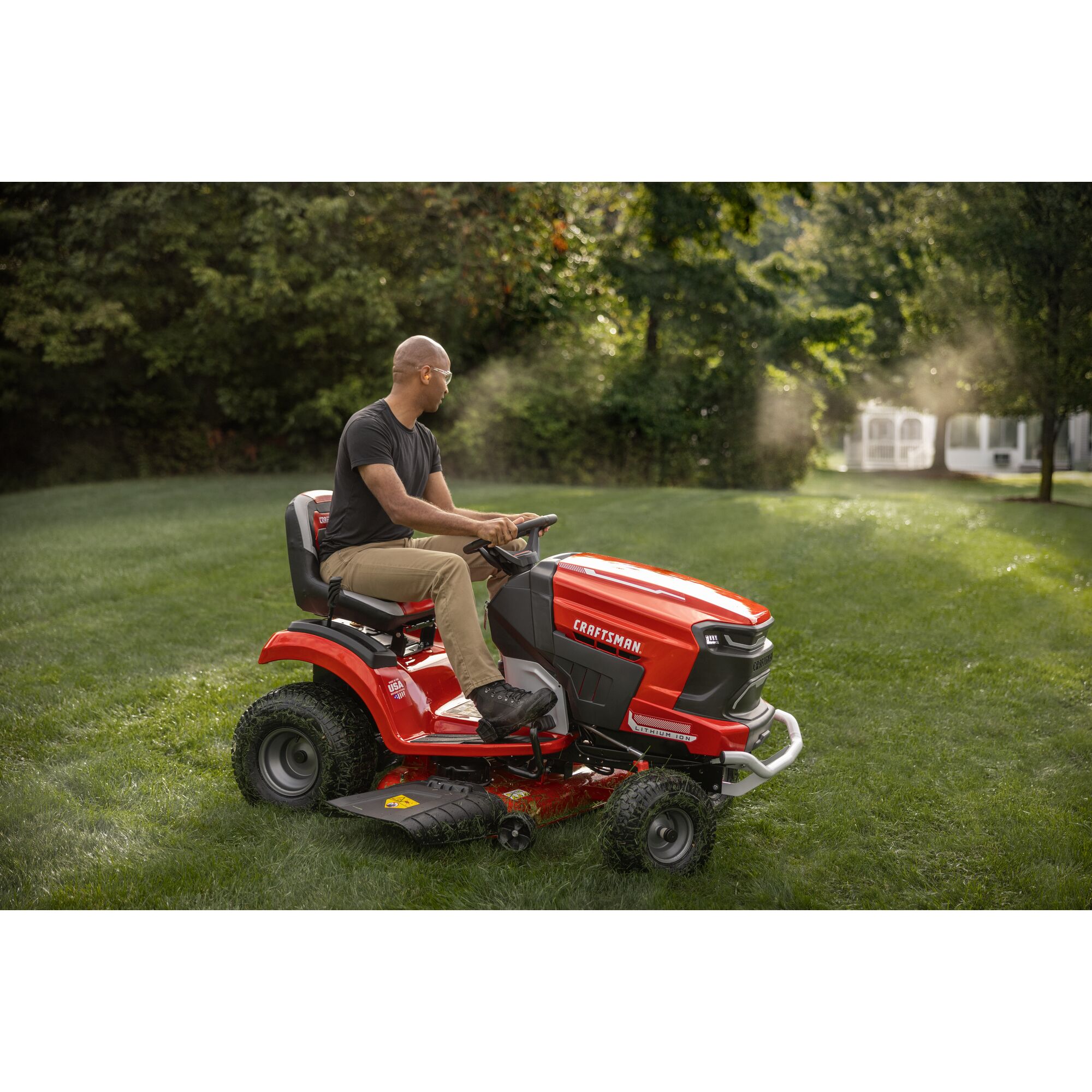 CRAFTSMAN Battery-Powered Riding Mower mowing background with woods and fence in background