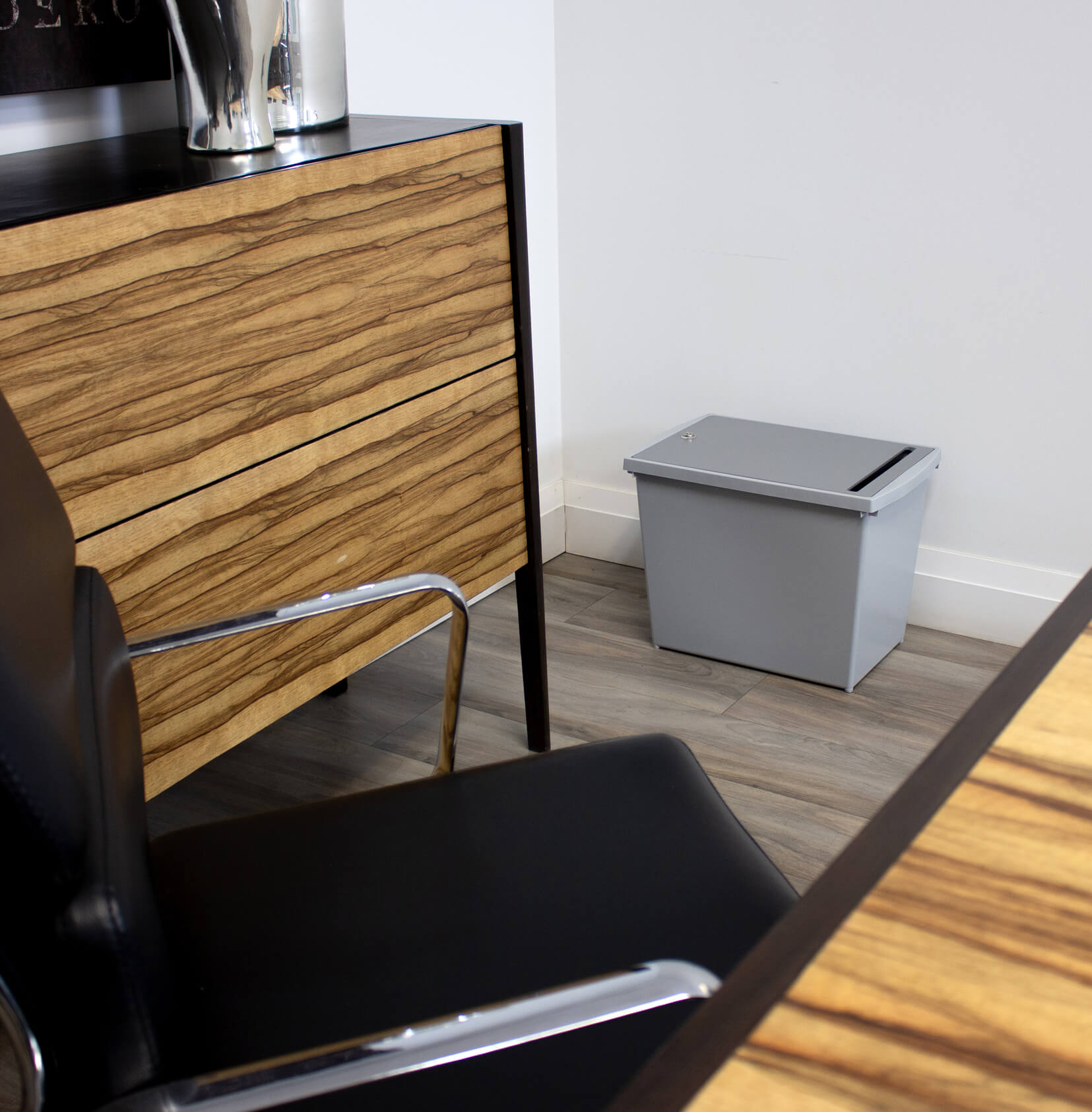 grey container for collecting personal documents with a lockable lid sitting on the floor in a meeting room