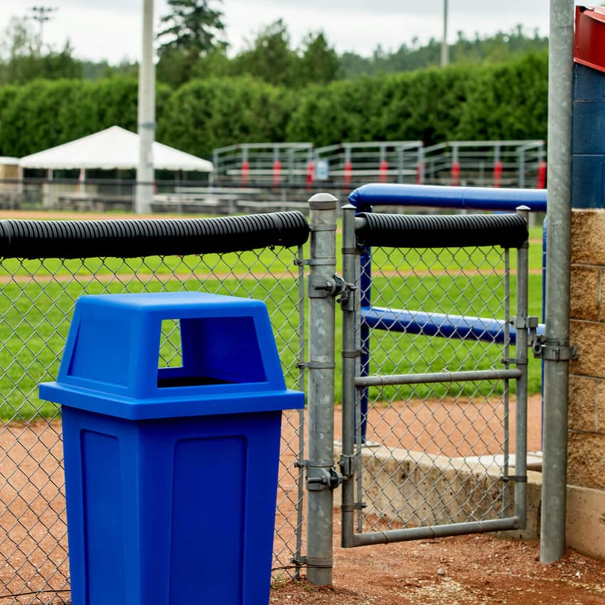 durable LDPE blue recycling bin with canopy lid sitting outside at a baseball diamond