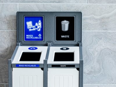 grey and white recycling plastic lumber waste and recycling container with a sign frame and labels against a marble wall in a high-end building lobby