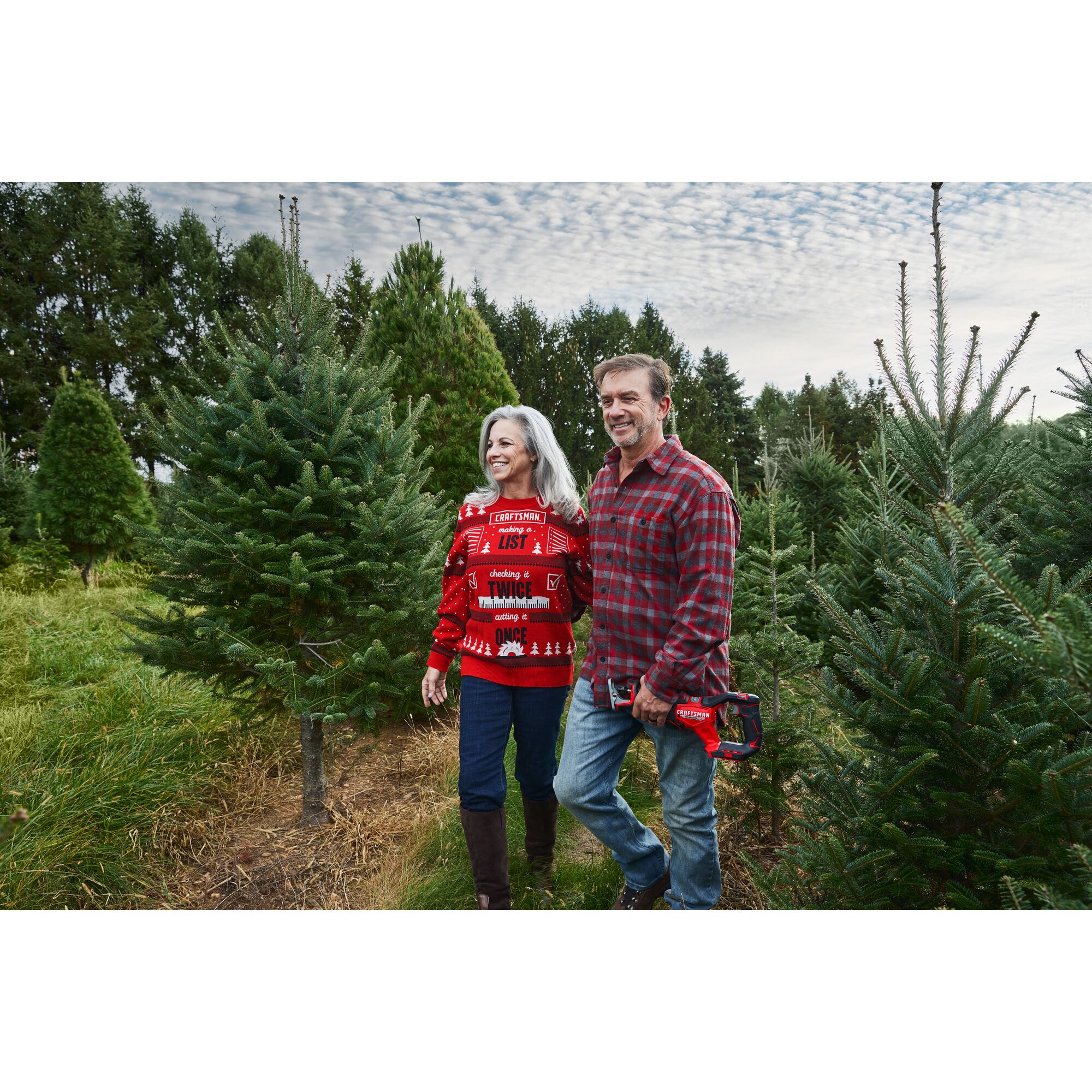 Female wearing CRAFTSMAN Holiday Sweater walking with male on Christmas tree farm