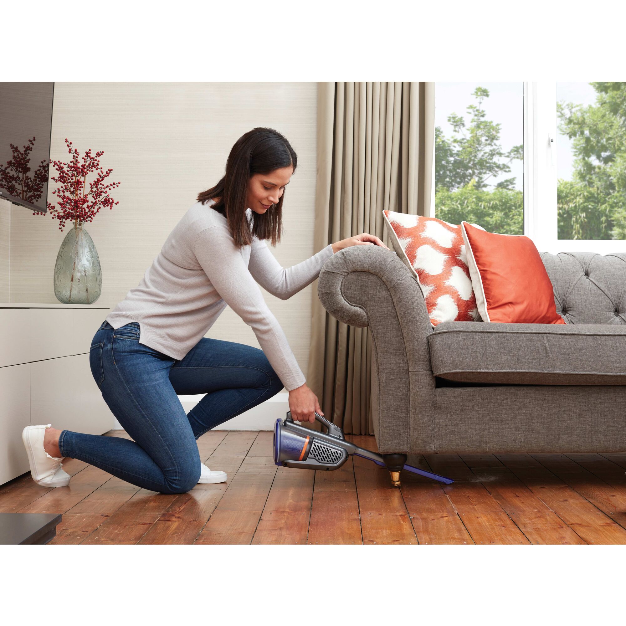 MAX Dustbuster Advanced Clean plus Pet Hand Vacuum With Base Charger and Extra Filter being used by person to clean wooden floor under sofa.