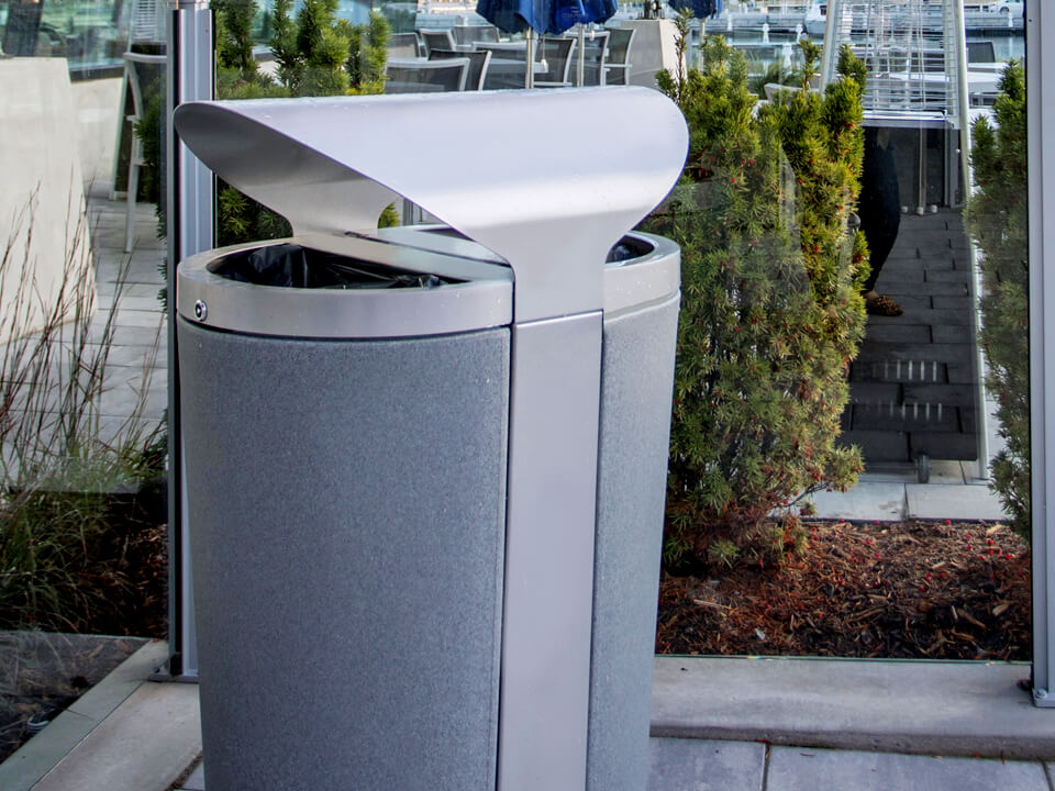 silver and grey metal outdoor waste and recycling bin with curved metal canopy lid and large plastic liners outside at an upscale marina